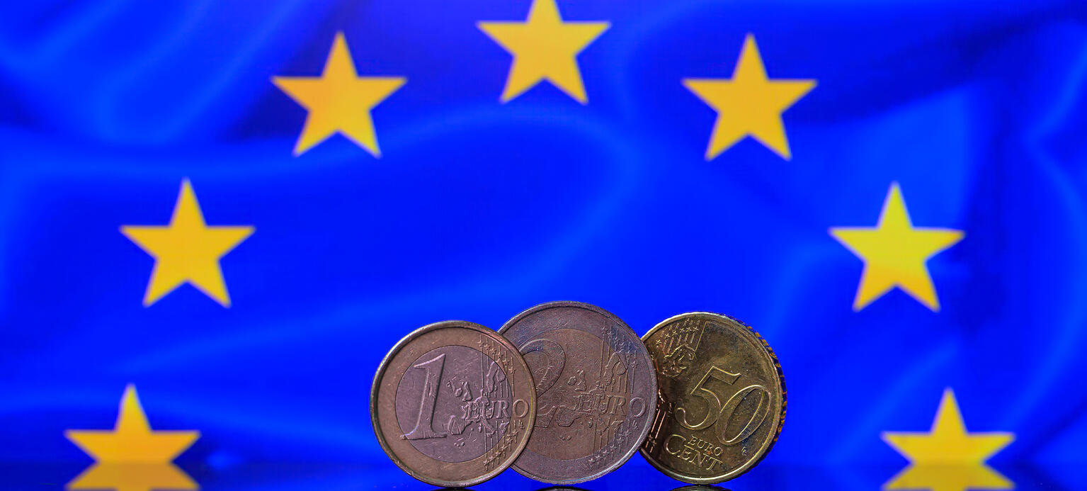 Drei Euromünzen werden auf einem Tisch gespiegelt und sind von den Sternen der Europäischen Flagge umgeben